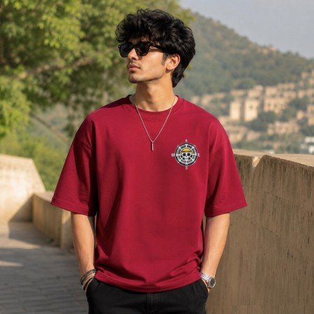 Male model wearing a maroon One Piece oversized t-shirt featuring a pirate emblem chest graphic and relaxed streetwear fit.