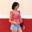 Side view of red and white gingham peplum top featuring ruffle sleeves and flared hem